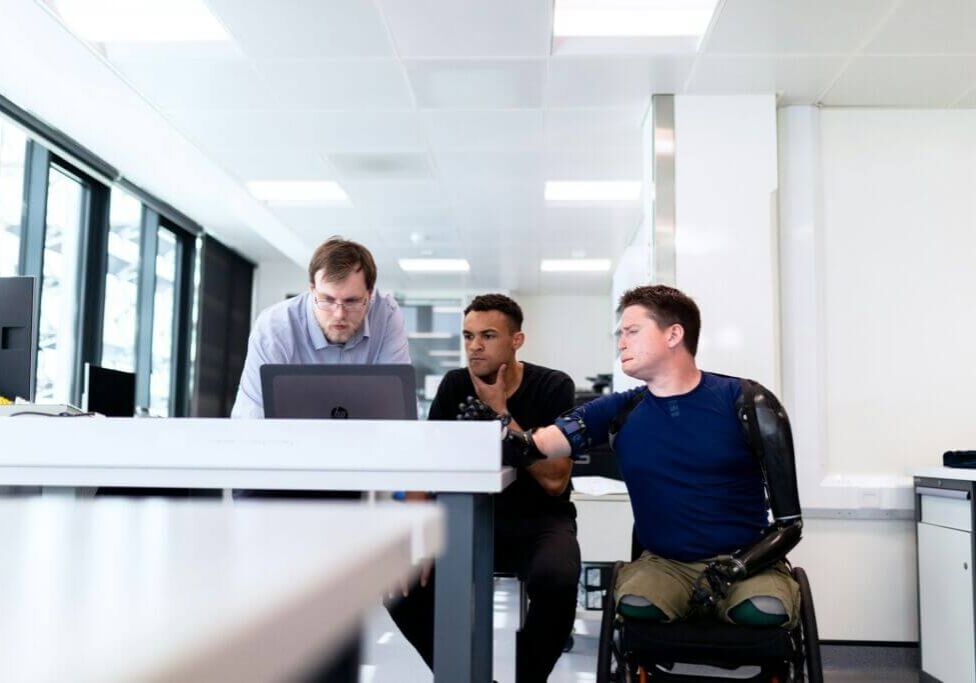 work-team-project-wheelchair-workforce-office-huddle Three people huddled around a laptop